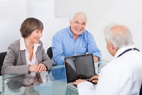 Happy Couple Discussing With Male Doctor