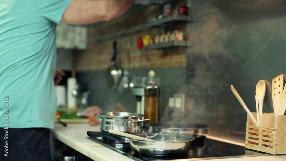 Man adding seasonings to meal on frying pan in the kitchen Man adding seasonings to meal on frying pan in the kitchen
