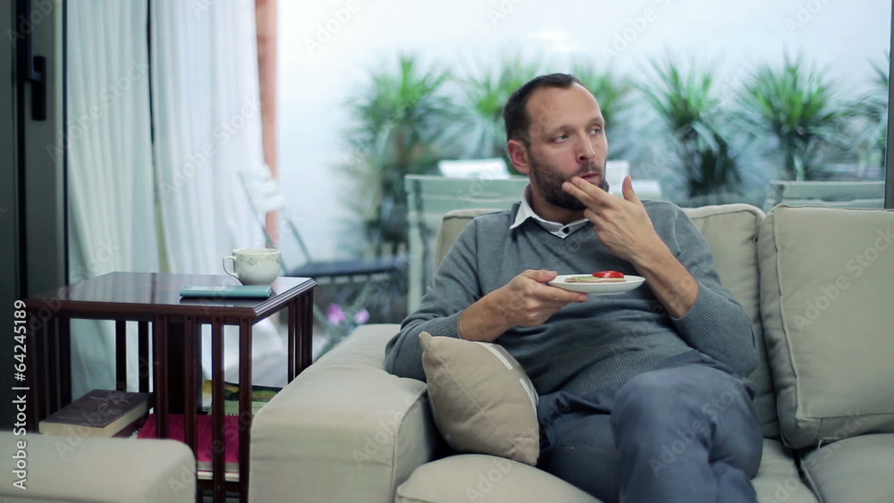 Man eating sandwich and drinking tea while sitting on sofa Man eating sandwich and drinking tea while sitting on sofa