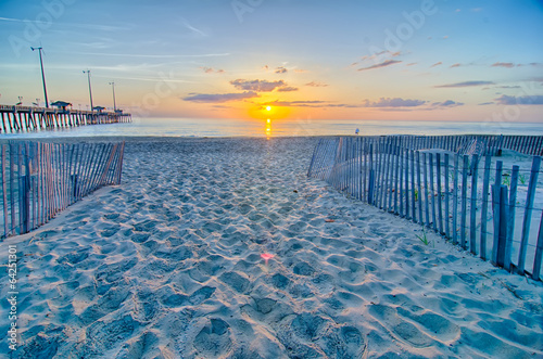 The rising sun peeks through clouds and is reflected in waves by photo