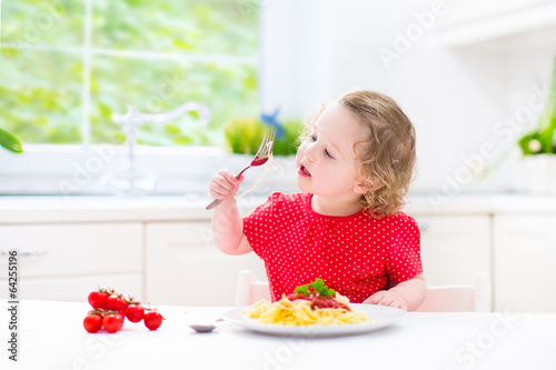 Adorable toddler girl eating spaghetti in white kitchen