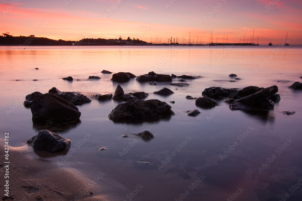 Sunset over boats with rocks in foreground
