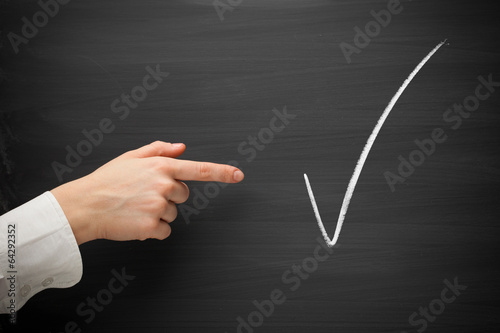 forefinger point at checkmark sign on a blackboard