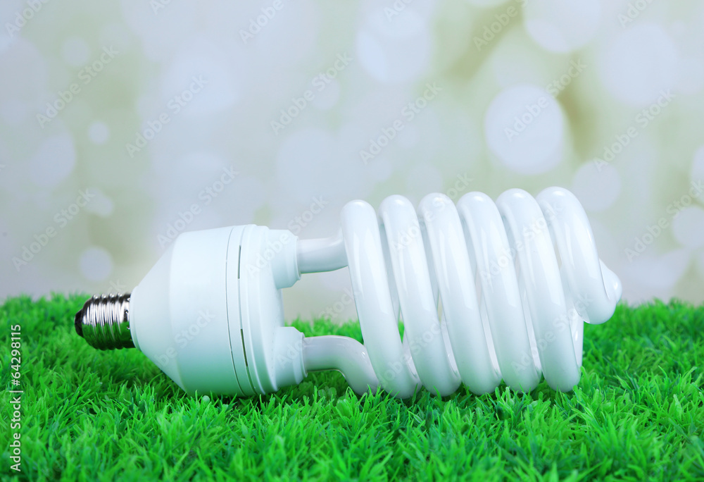 Energy saving light bulb on green grass, on light background