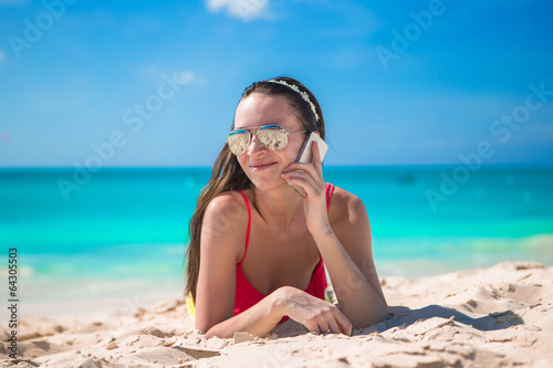 Young woman lying on white sand and talking by her phone