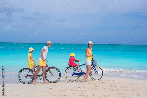 Young parents and little girls with bikes on a tropical white