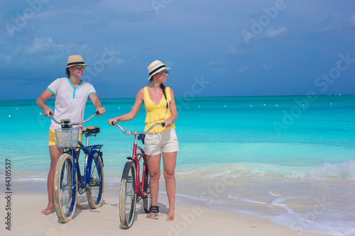 Young happy pair riding bikes on white tropical beach