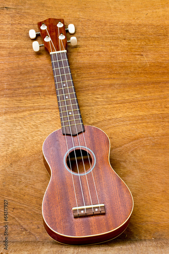 The ukulele is placed on a wooden floor.