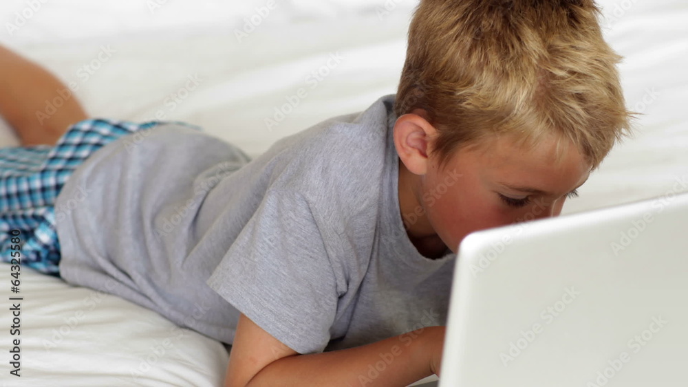 Little boy using laptop on bed