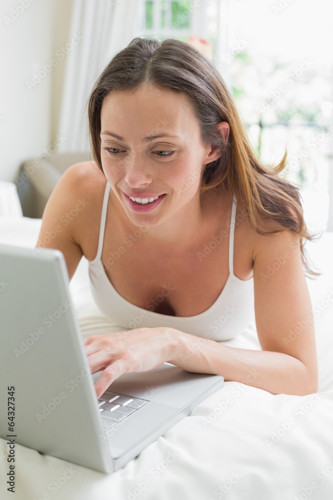 Smiling relaxed woman using laptop in bed Smiling relaxed woman using laptop in bed