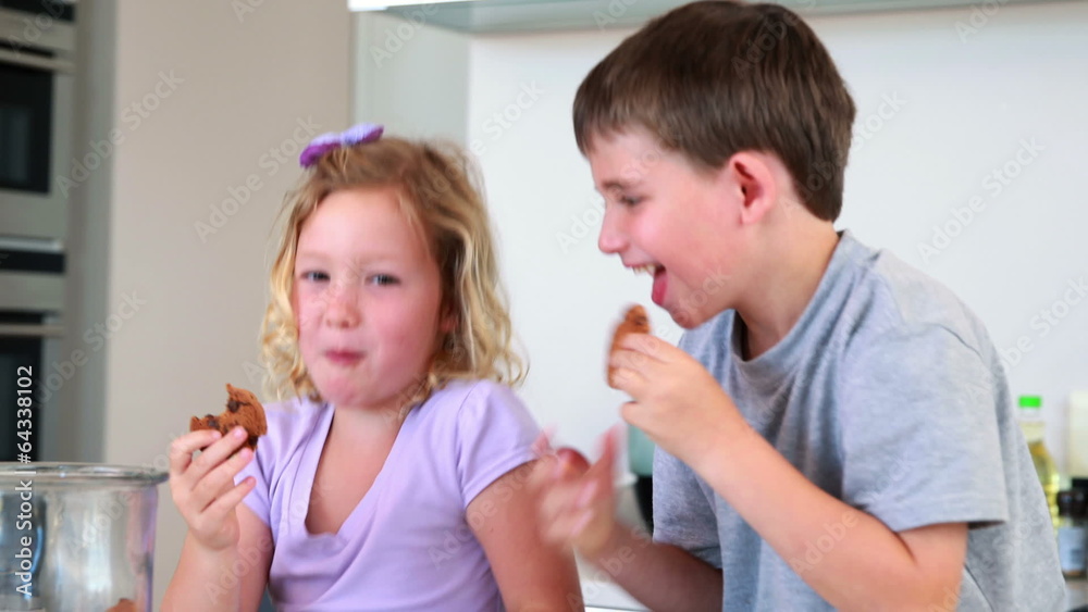 Siblings taking cookies from the jar and eating them Siblings taking cookies from the jar and eating them