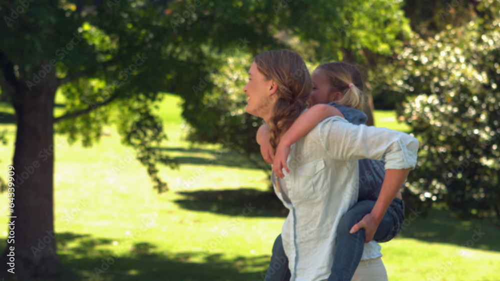 Young mother giving her daughter a piggy back in the park Young mother giving her daughter a piggy back in the park