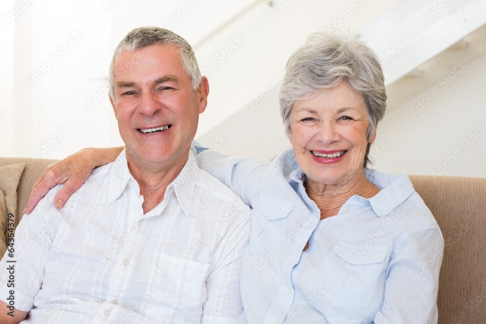 Retired couple sitting on couch smiling at camera Retired couple sitting on couch smiling at camera