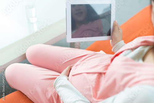 Happy pregnant woman looking at camera, using a digital tablet