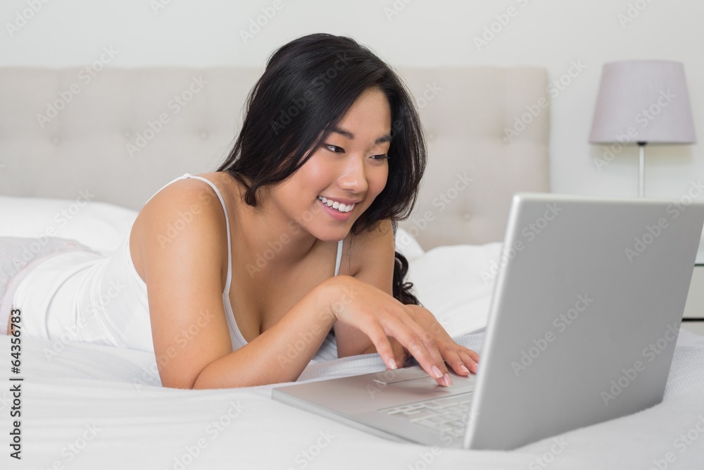 Happy woman lying on bed using laptop Happy woman lying on bed using laptop