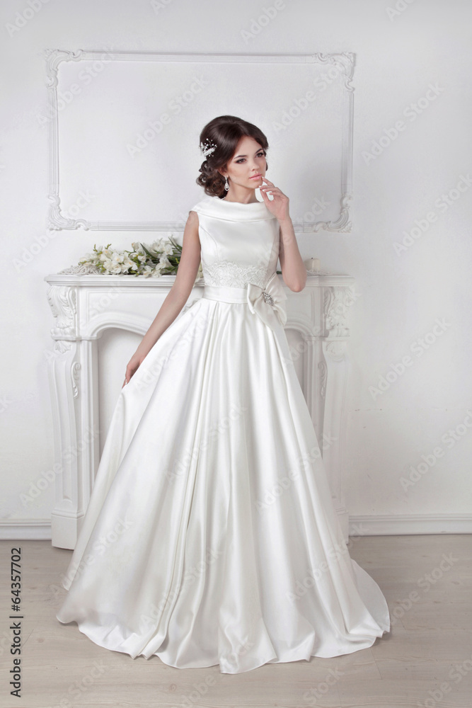 Beautiful bride woman posing in magnificent dress over white wal
