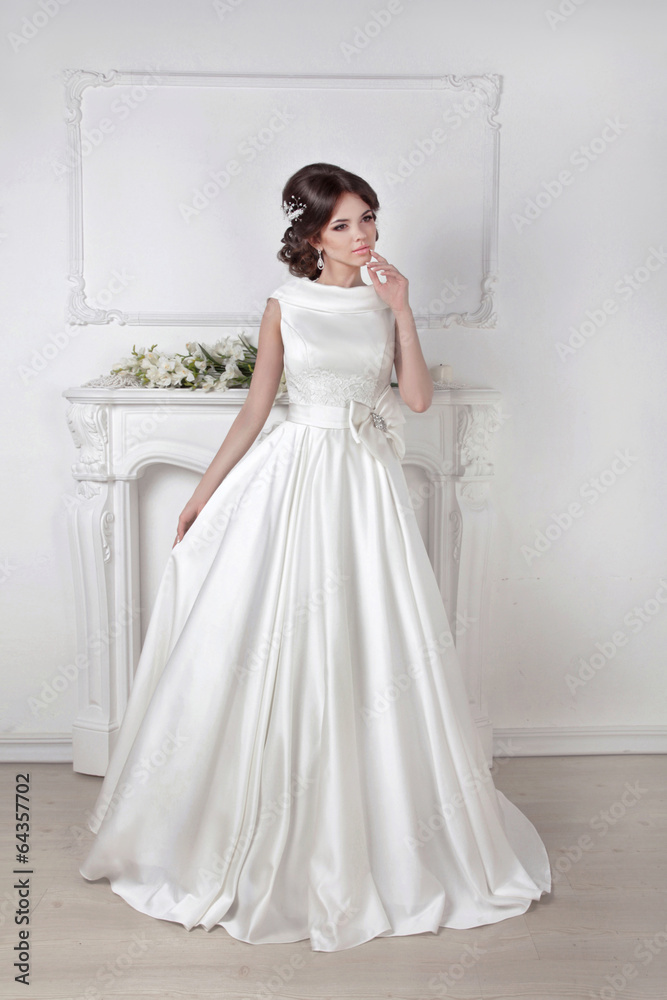 Beautiful bride woman posing in magnificent dress over white wal Beautiful bride woman posing in magnificent dress over white wal