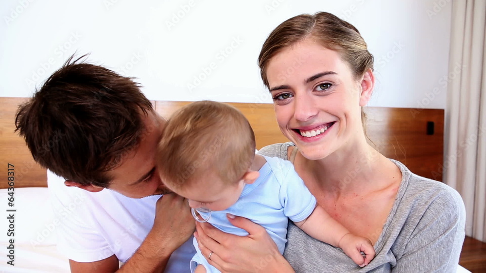 Happy parents sitting on bed with their baby son Happy parents sitting on bed with their baby son