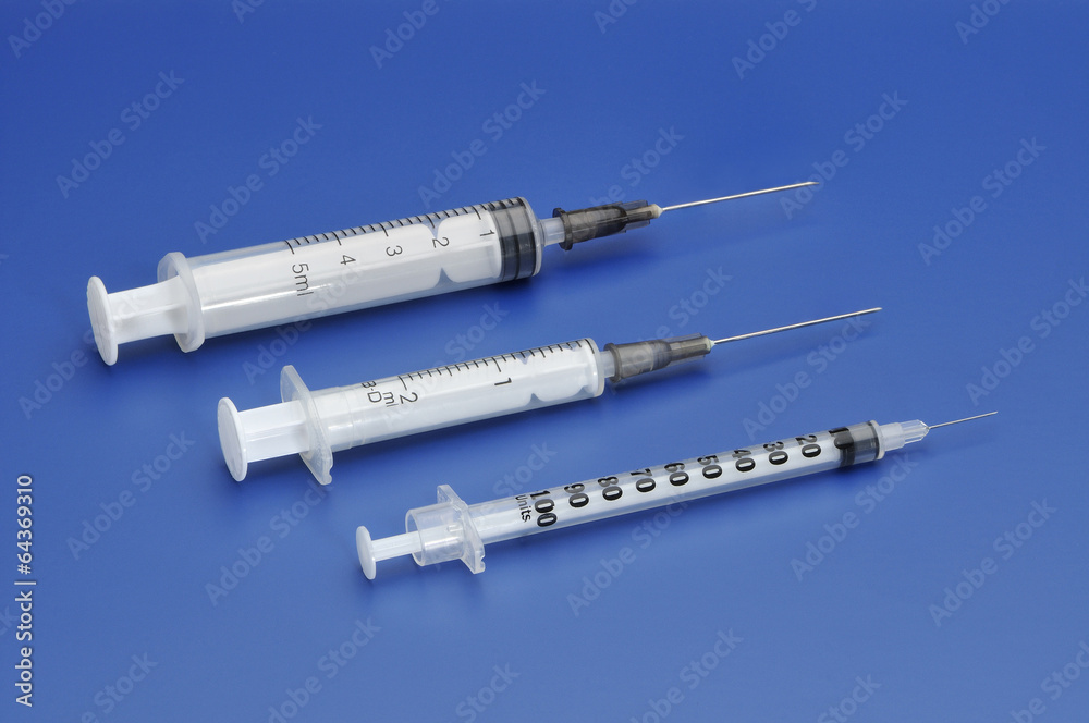 Three plastic disposable syringes with a needle on blue backgrou Three plastic disposable syringes with a needle on blue backgrou