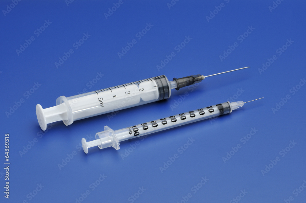 Two plastic disposable syringes with a needle on blue background