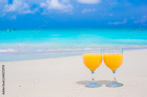 Two glasses of orange juice on tropical white beach