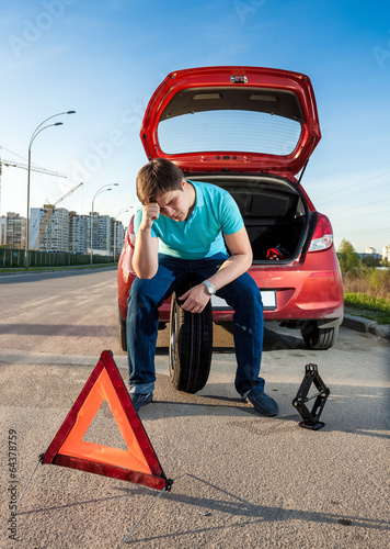 man sitting on spare wheel near broken car