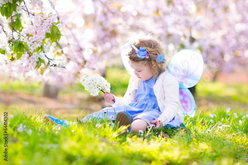 Little toddler girl in fairy costume in fruit cherry garden