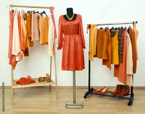 Wardrobe closet with orange clothes on hangers and mannequin.