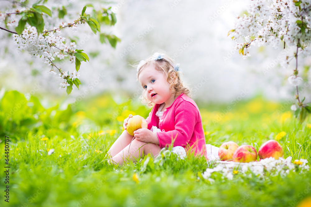 Swet toddler girl eating apple in blooming garden Swet toddler girl eating apple in blooming garden
