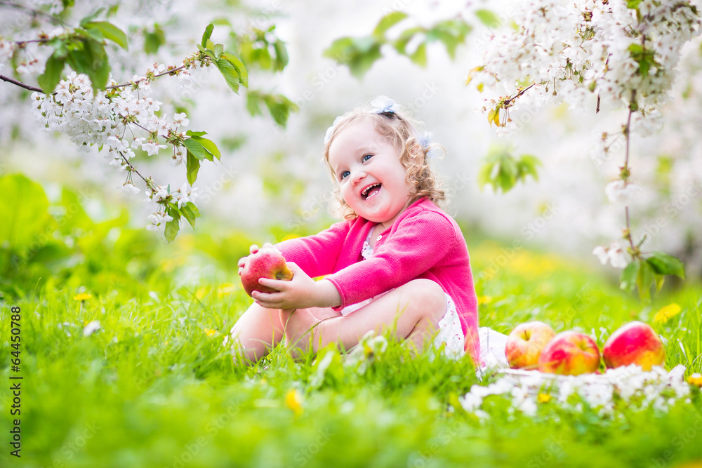 Adorable toddler girl eating apple in blooming garden Adorable toddler girl eating apple in blooming garden