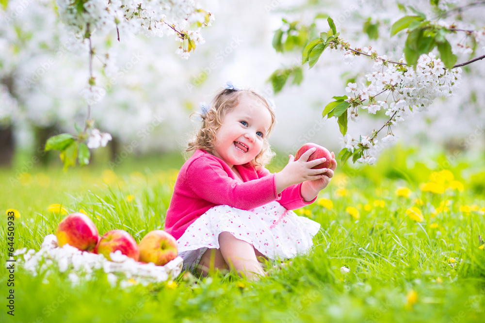 Happy toddler girl eating apple in blooming garden Happy toddler girl eating apple in blooming garden