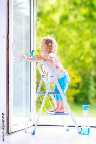 Sweet toddler girl washing a window with view garden © famveldman