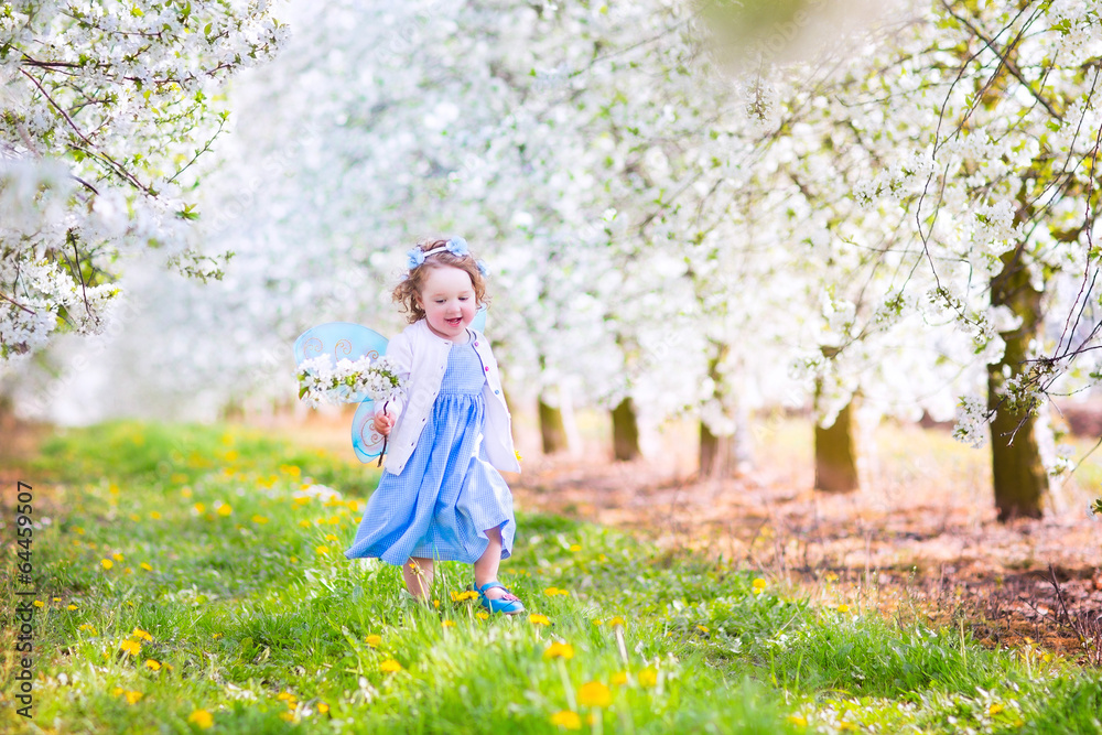 Cute toddlger girl in fairy costume playing in a blooming garden
