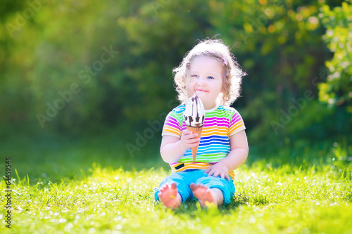 Pretty toddler girl eating ice cream in a sunny garden