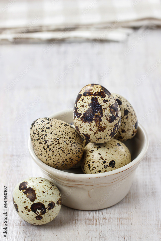 Obraz premium Quail eggs in ceramic bowl standing on rustic wooden table