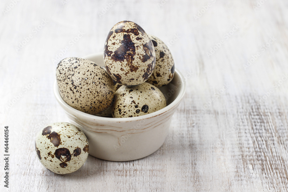 Obraz premium Quail eggs in ceramic bowl standing on rustic wooden table
