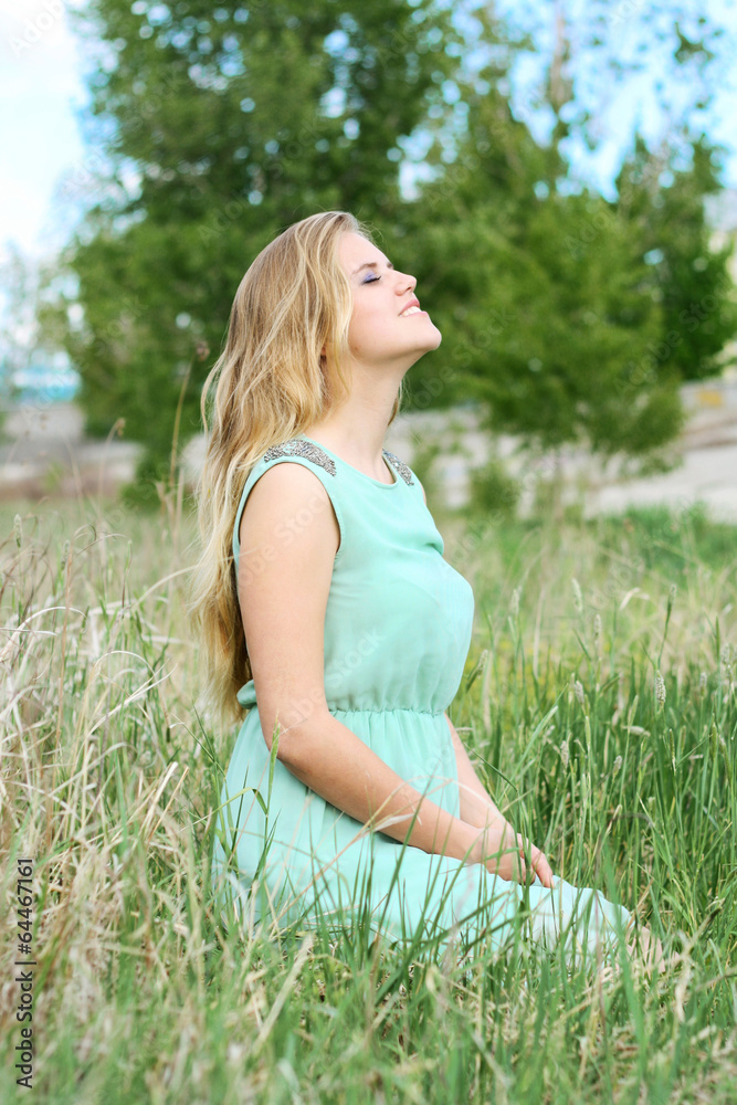 gorgeous woman sitting grass in dress with head raised to  sky