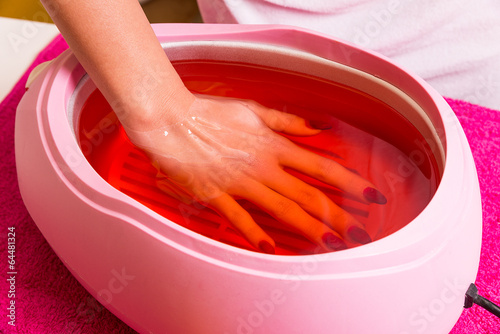 Fototapeta Female hand and orange paraffin wax in bowl.