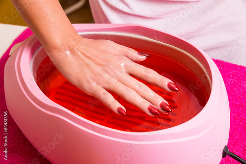 Fotografiet Female hand and orange paraffin wax in bowl.