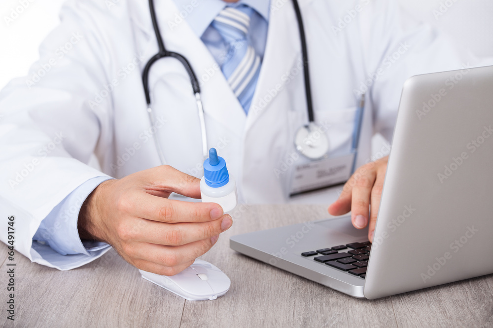 Doctor Holding Drop Bottle While Using Laptop Doctor Holding Drop Bottle While Using Laptop