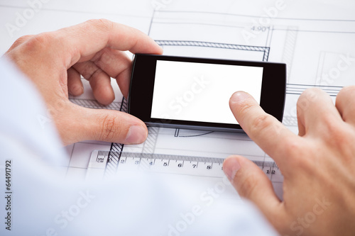 Architect Touching Smartphone's Screen Over Blueprint