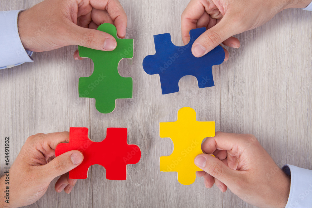 Businesspeople Joining Multicolored Puzzle Pieces At Desk Businesspeople Joining Multicolored Puzzle Pieces At Desk
