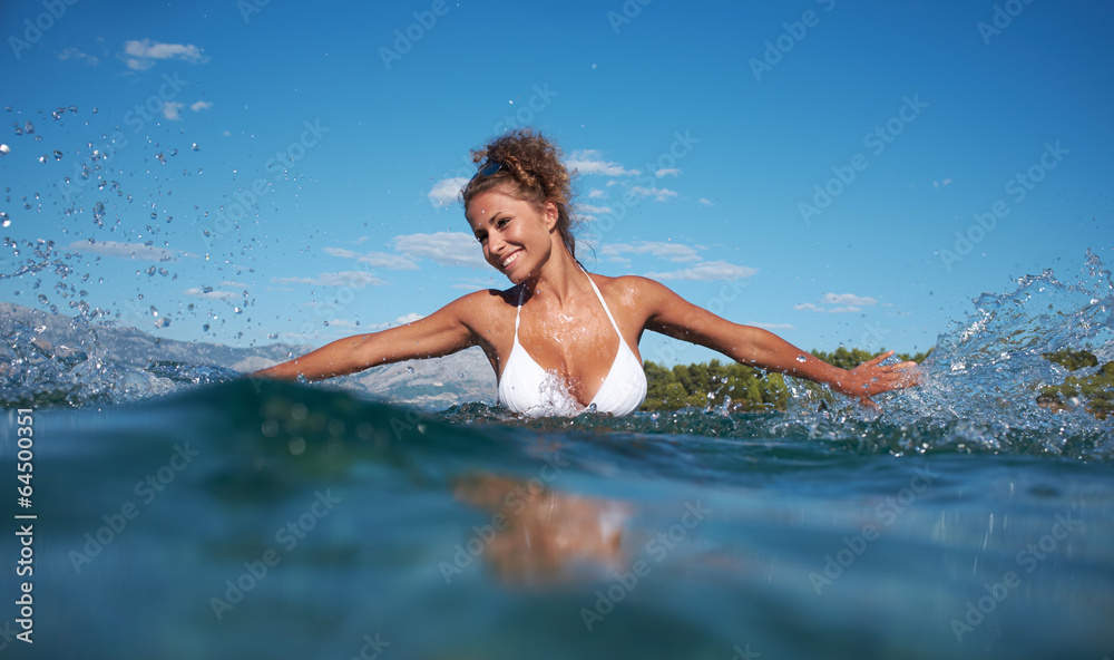 Beautiful young woman in bikini on the beach splashing water