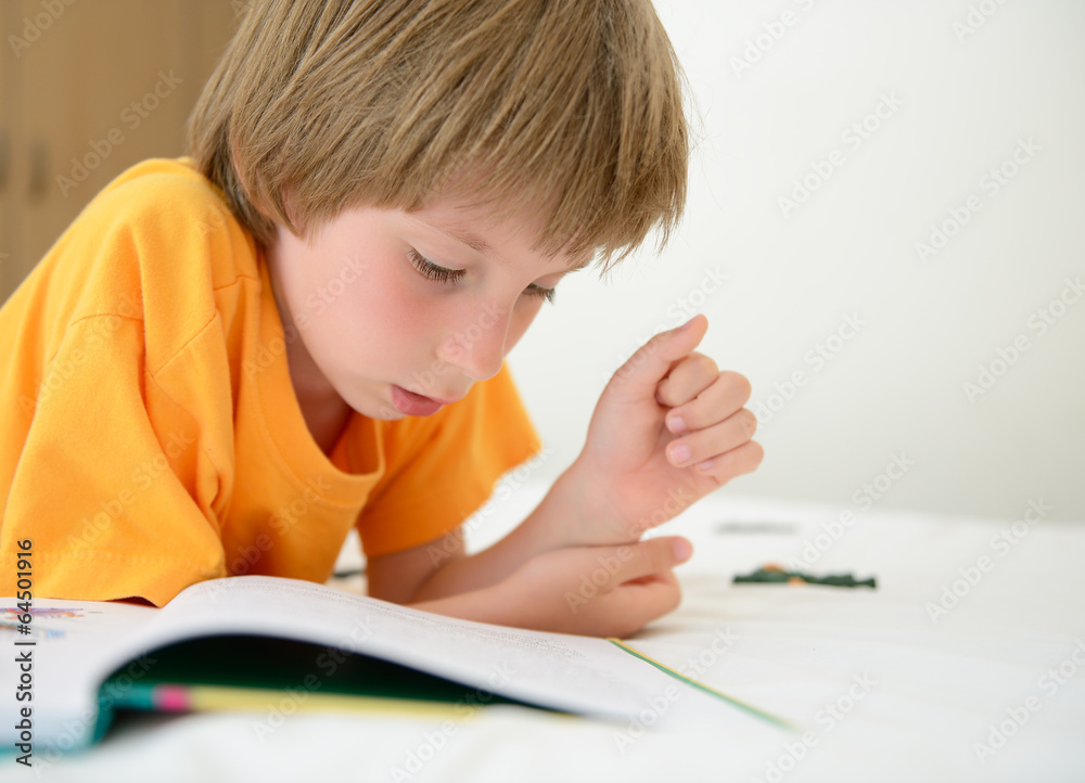 little boy reading book with interest lying on bed in his room little boy reading book with interest lying on bed in his room