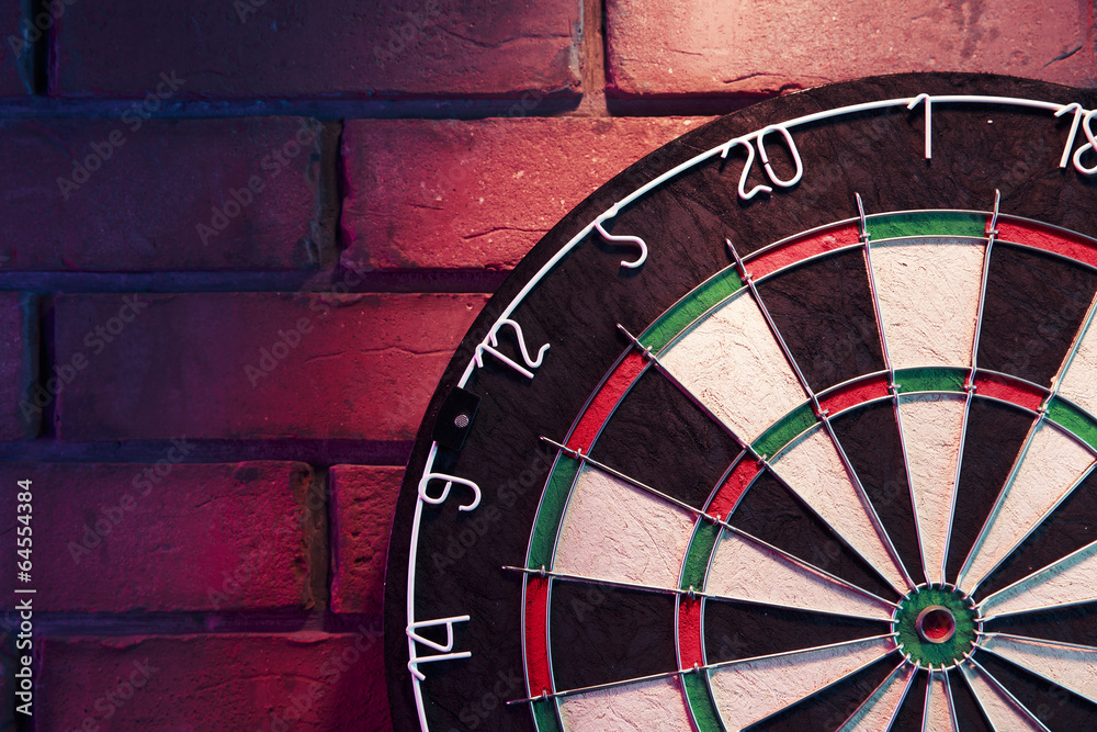 Naklejka premium Dart board on a brick wall with dramatic lighting