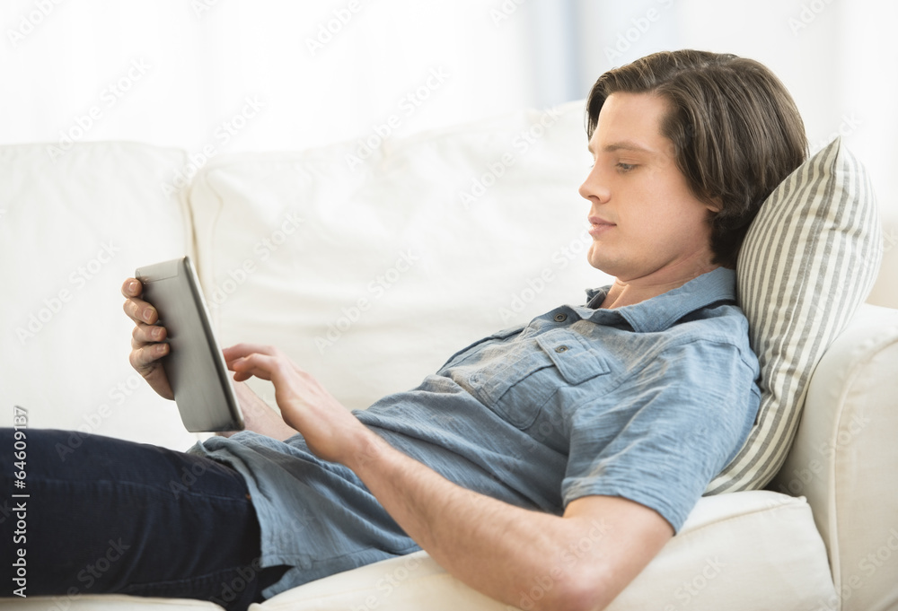 Obraz premium Man Using Digital Tablet While Lying On Sofa