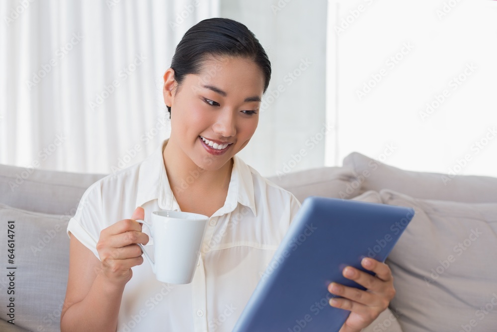 Smiling woman sitting on couch using tablet pc having coffee Smiling woman sitting on couch using tablet pc having coffee