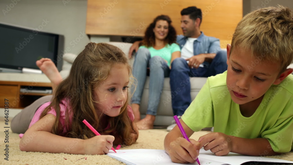 Siblings colouring on the floor while their parents are sitting Siblings colouring on the floor while their parents are sitting