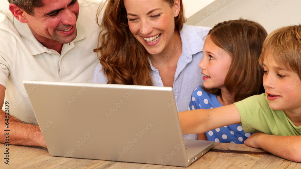 Smiling family using laptop together at table Smiling family using laptop together at table