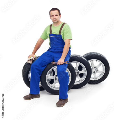Friendly car mechanic sitting on tires